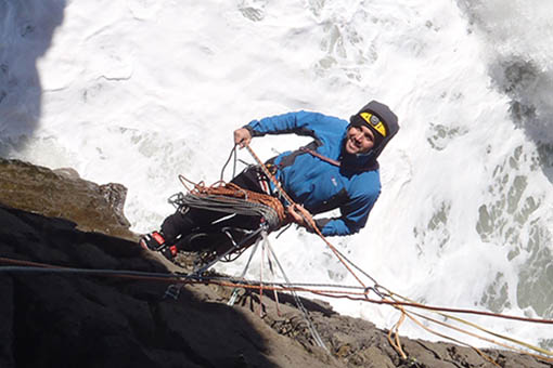 A small image of a climber hanging on a cliff above the crashing waves