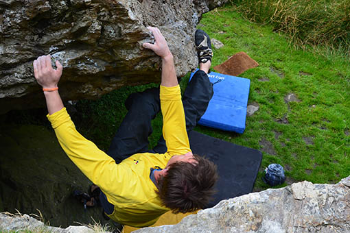 A large image of a climber climbing holding onto a boulder with his heels
