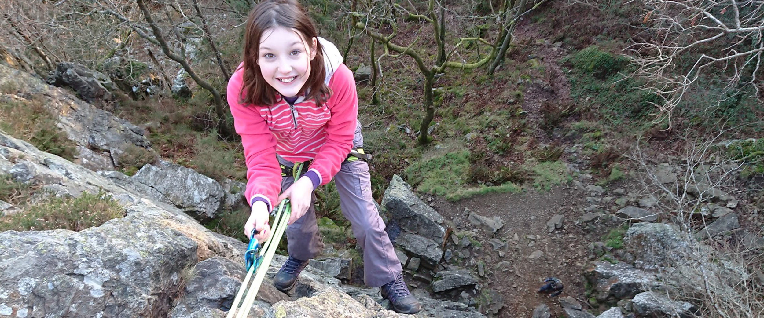 A confident child rock climber, hanging by a rope over the edge of a cliff