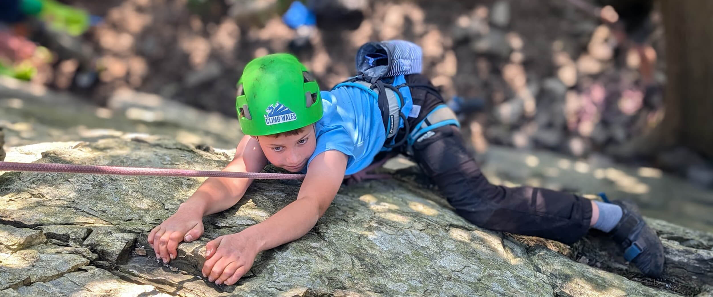 A young boy climbing a cliff face with a look of concentration