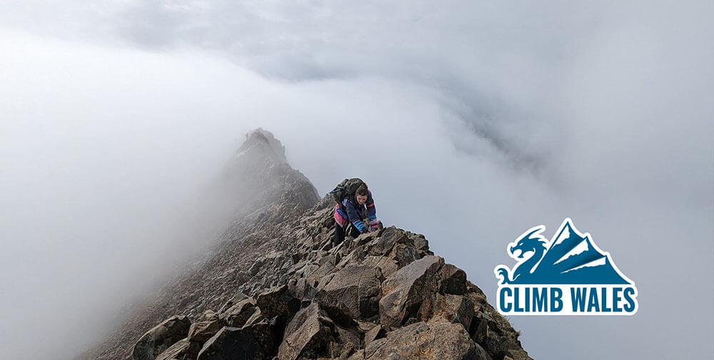A lady crawls across Crib Goch whose ridge disappears into the clouds