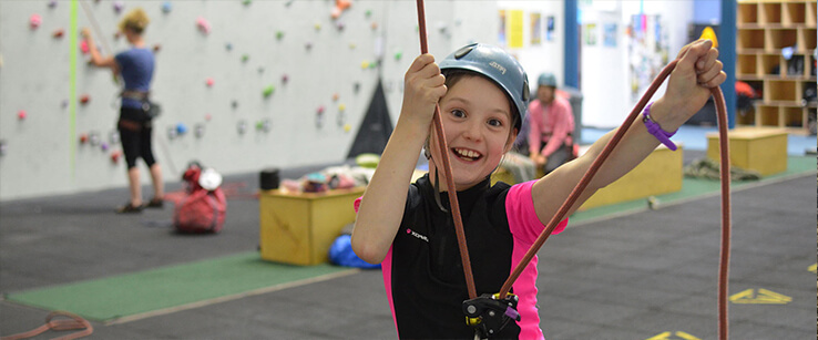A very happy child holds a rope at an indoor climbing wall