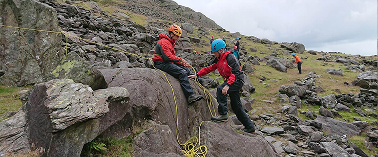 Two mountaineers perched on some boulders demonstrate scrambling rope work